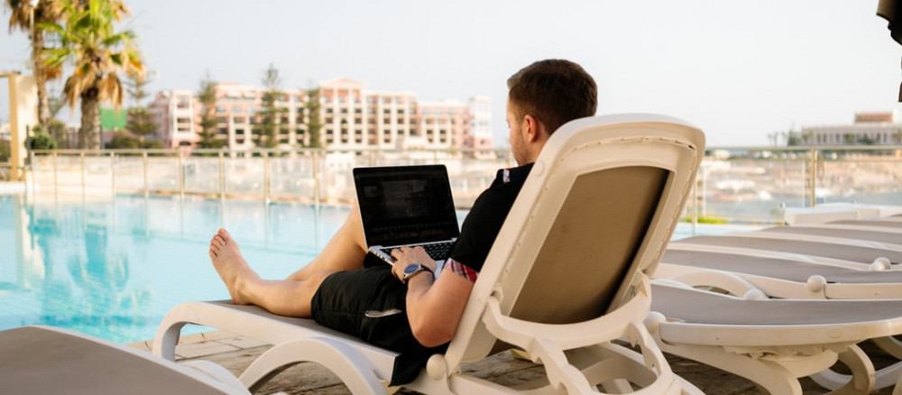 Man sitting at the pool holding a laptop